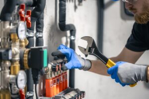 A man installs a heating system in a house and checks the pipes with a wrench.